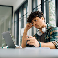 Ein junger Mann sitzt in einer Bibliothek und arbeitet an einem Laptop.