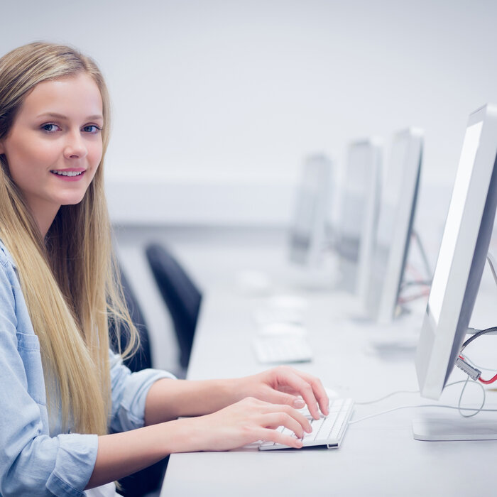 Eine junge Studierende sitzt in einem Computerraum und schaut von ihrer Tastatur auf. 